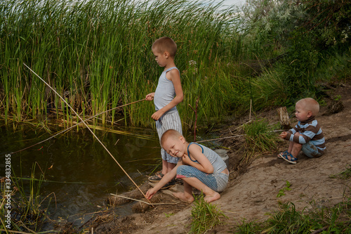 Funny children in colorful clothes took fishing rod and try to fish near river in the reeds. Funny situations while fishing. Summer vacation in village. Brothers are happy together © galitsin