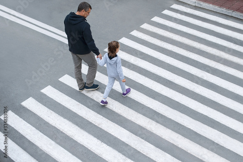 Man and child on a zebra crossing trespassing by crossing the street. In the summer on the street kid girl with her father in fashion clothes cross the road. From top view. Traffic rules for children