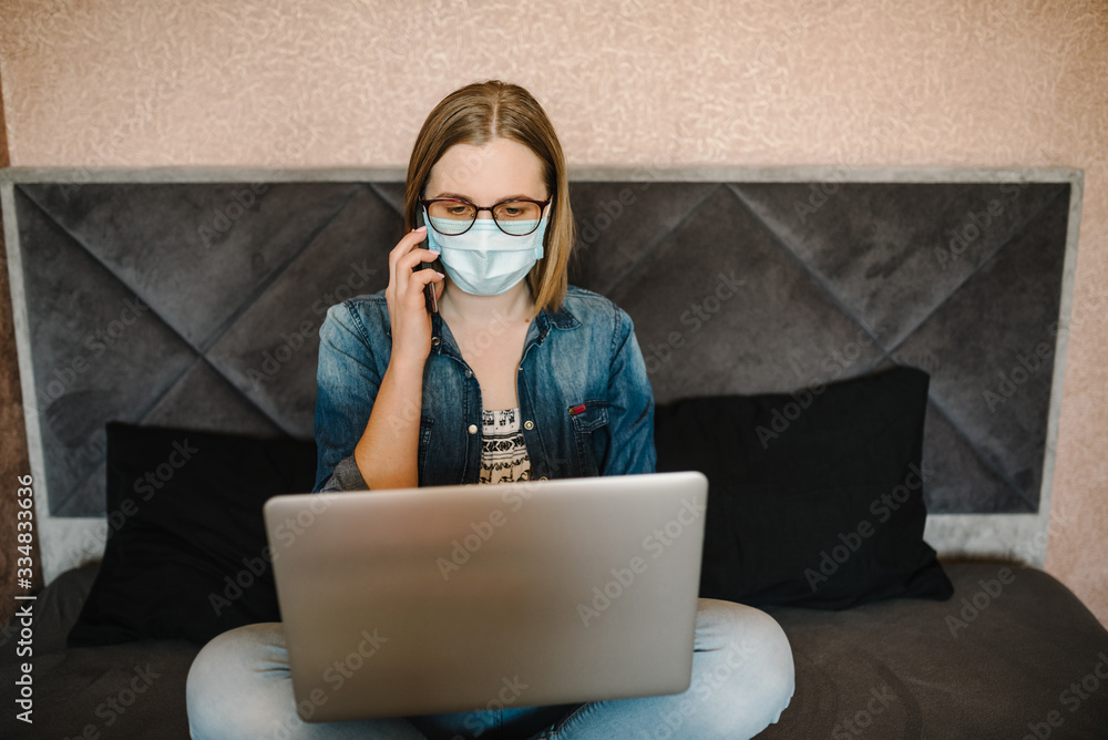 Coronavirus. Business woman working in home, wearing protective mask in quarantine. Stay at home. Girl learns, talking on phone, using laptop computer in bedroom. Freelance. Writing, typing. Coronavirus. Business woman working in home, wearing protective mask in quarantine. Stay at home. Girl learns, talking on phone, using laptop computer in bedroom. Freelance. Writing, typing.