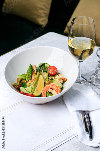 Salad with shrimp, cucumber, olives, tomatoes and basil. Glass of white wine. Place for text