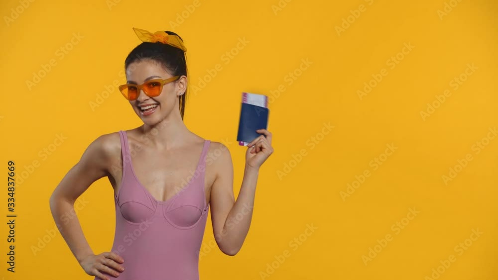 Smiling girl in swimsuit pointing on passport and air ticket isolated on yellow Smiling girl in swimsuit pointing on passport and air ticket isolated on yellow