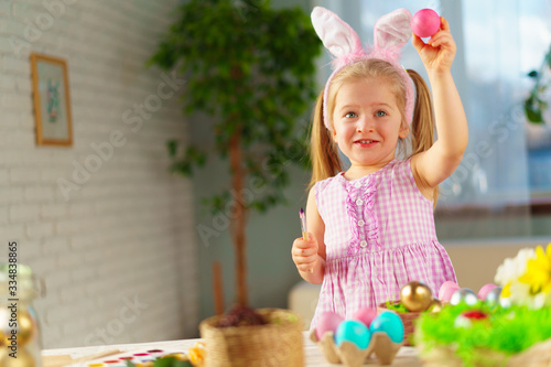 Toddler girl with bunny ears coloring eggs for Easter