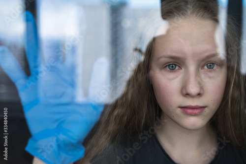 portrait of a young girl with bliues eyes near window with surgical gloves coronavirus protection