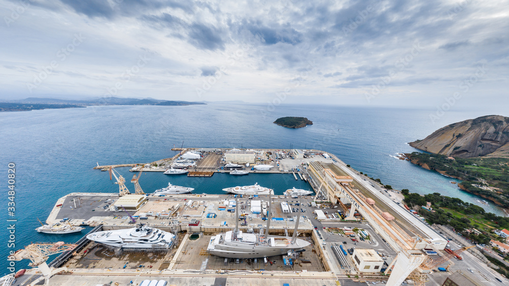 Aerial view of sea dry dock in La Ciotat city, France, the cargo crane, boats on repair, a luxury sail yacht and motor yacht, mountain is on background, shipyard