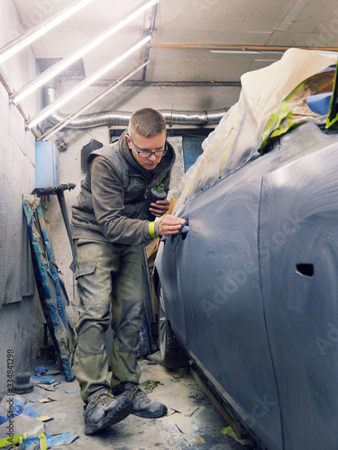 cheerful, young man with glasses polishes, primes and paints a car in the garage