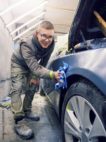 cheerful, young man with glasses polishes, primes and paints a car in the garage