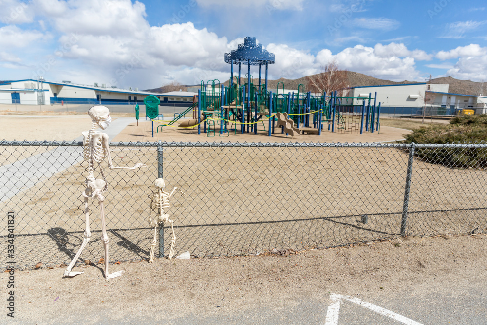 Adult and child skeleton behind fence looking at an empty closed park on a nice day
