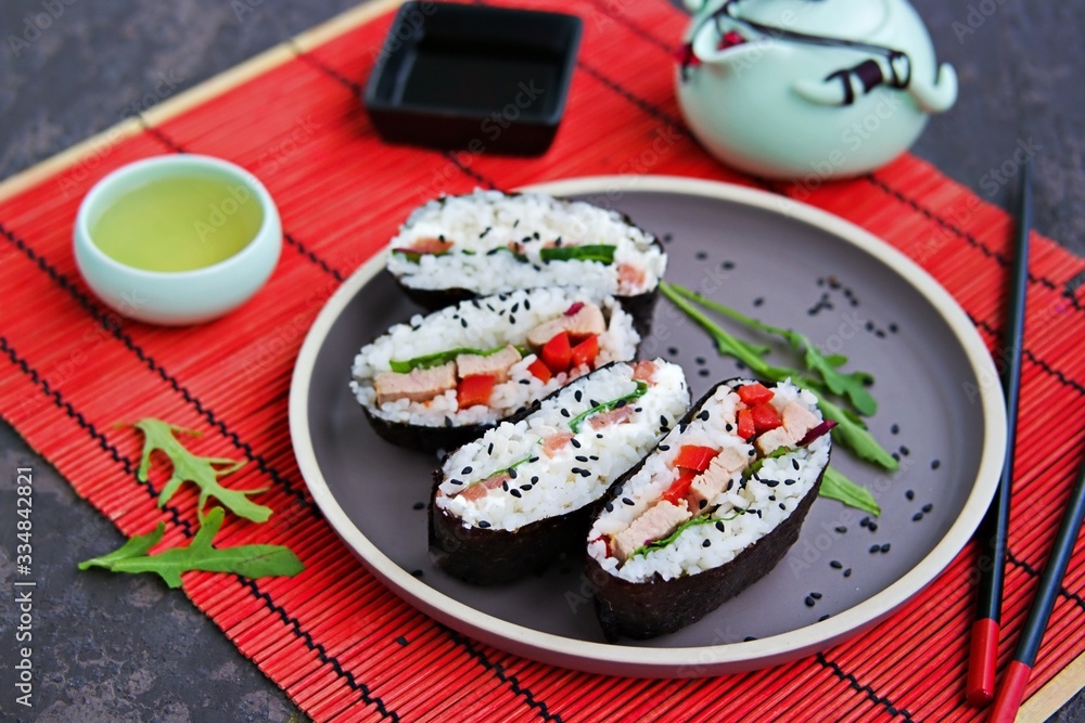 Assorted sushi sandwiches onigirazu with baked duck, spinach and sweet pepper and with salmon and cream cheese on a brown clay plate on a dark concrete background. Japanese food. Assorted sushi sandwiches onigirazu with baked duck, spinach and sweet pepper and with salmon and cream cheese on a brown clay plate on a dark concrete background. Japanese food.