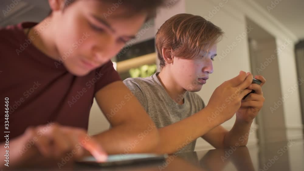 Teenage boys with smartphones at home. Two boys spending time in a social network using mobile phones. White teenagers using cell phones for gaming. Young people with phones. Teenage boys with smartphones at home. Two boys spending time in a social network using mobile phones. White teenagers using cell phones for gaming. Young people with phones.