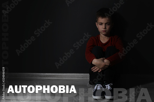 Sad little boy sitting alone near black wall, space for text. Autophobia photo