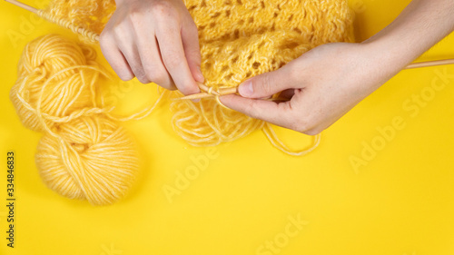 Women's hands knit from yellow wool on a yellow background, top view. Hand knitting