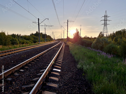 Railroad rails and electric wires in the summer on sunset background