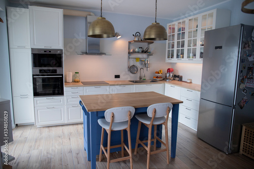 White, scandinavian kitchen with blue island and double brass pendant lights.