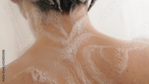 Naked woman takes a shower. Woman washes her short hair with shampoo. Slow motion video in white bathroom.