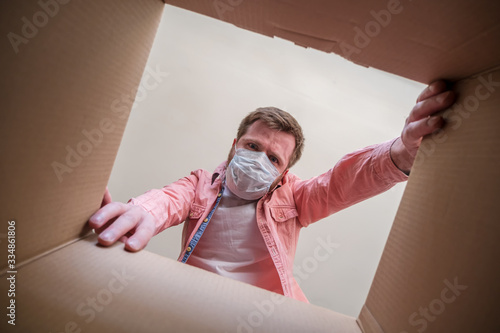 Tablou pe pânză Man in a medical mask unboxing inside view a delivered box