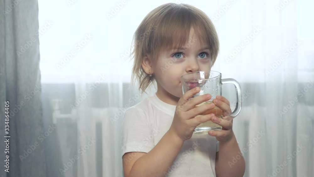 little girl drinks juice indoors. girl sister drinks lemonade from a lifestyle glass little girl drinks juice indoors. girl sister drinks lemonade from a lifestyle glass