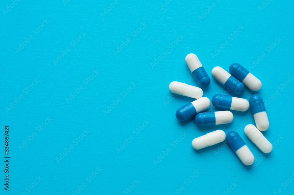 Antiviral capsules, pills for treatment on a blue background. White-blue capsules. Flat lay, top view Antiviral capsules, pills for treatment on a blue background. White-blue capsules. Flat lay, top view