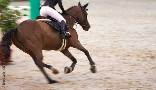 A rider on a beautiful brown horse rides around obstacles, motion blur, focus on the rider's boot