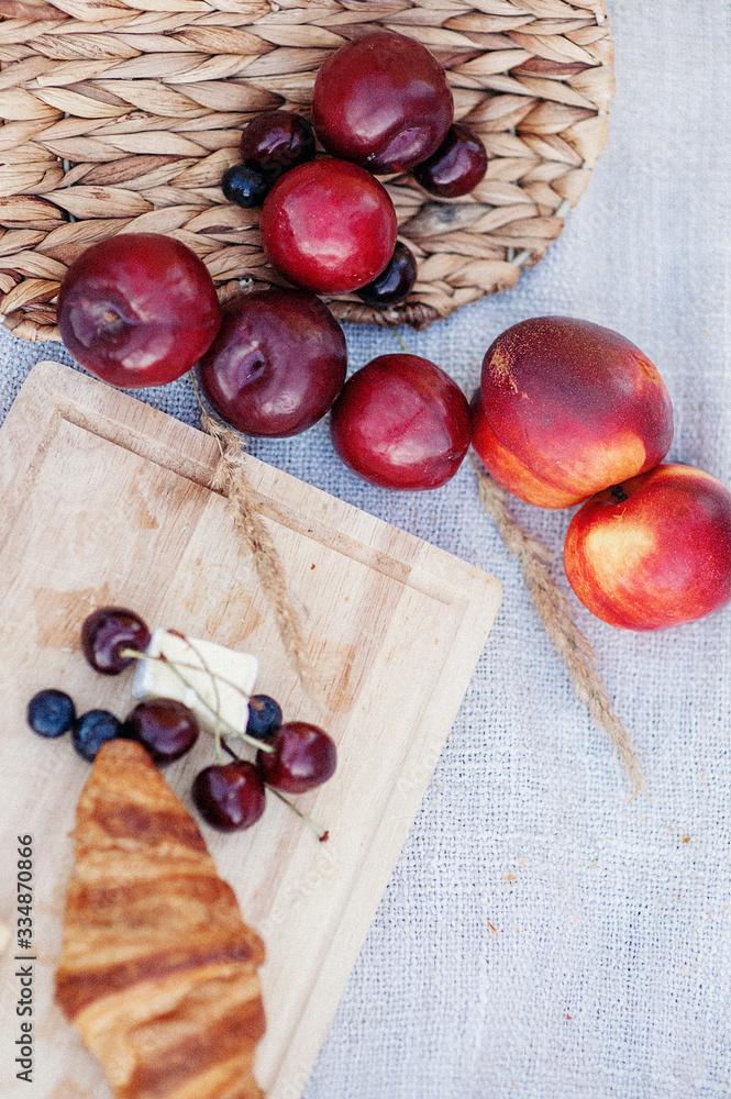 croissant, cherries, currants, cheese and spikelets on a wooden board. Next to them lie nectarines and plums.