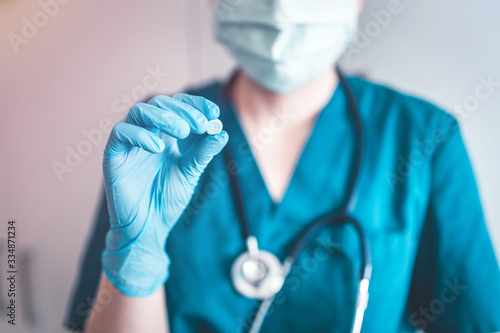Doctor holding a pill, looking at it and giving it as a treatment to the patient