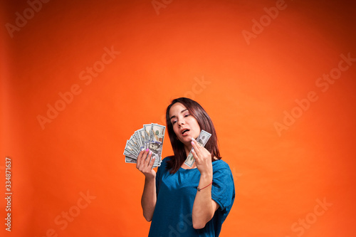 Young woman holding money in both hands on orange background