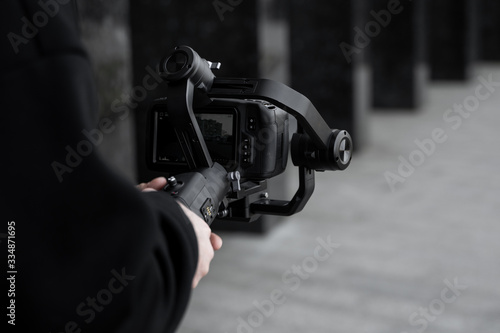 Professional videographer in black hoodie holding professional camera on 3-axis gimbal stabilizer. Filmmaker making a great video with a professional cinema camera. Cinematographer. photo