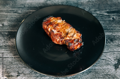 A black plate with one smoked pork chop from an outdoor barbecue grill smoker for a dinner meal