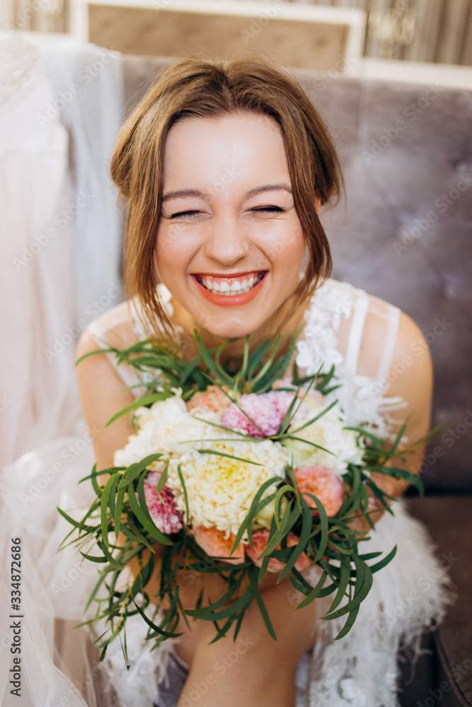 A funny bride with a bouquet in her hands sits on a soft chair in the room. A funny bride with a bouquet in her hands sits on a soft chair in the room.