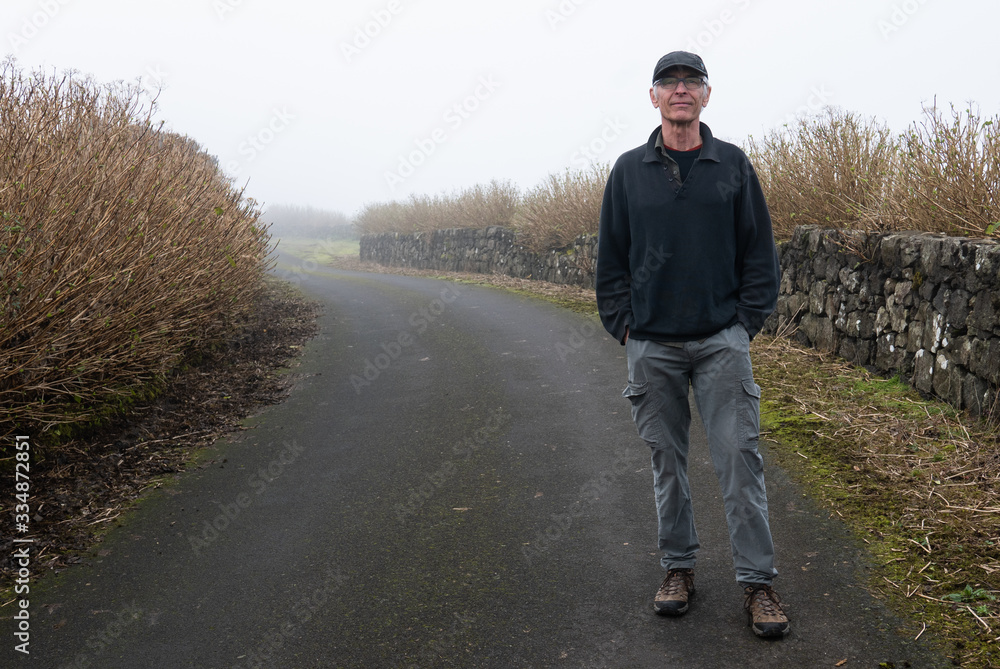 Handsome senior man walking on path with rock wall and foliage on a foggy day Handsome senior man walking on path with rock wall and foliage on a foggy day