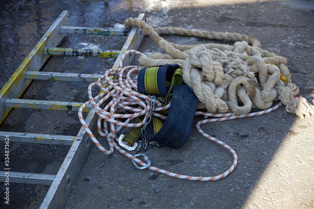 Equipment consisting of a ladder, ropes and a safety belt for working at high altitude lies on the asphalt.
