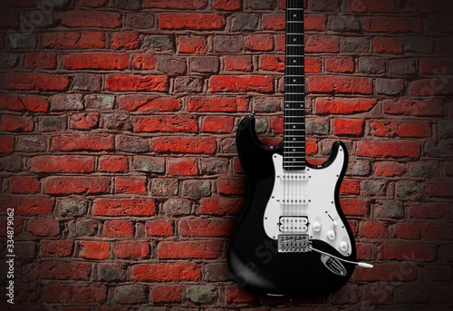 Black electric guitar on red brick wall background © SlayStorm