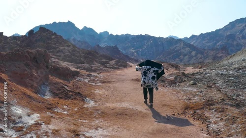 Rear back shot of a lonely woman with a scarf walking alone in a surrealistic colorful mountainous way photo