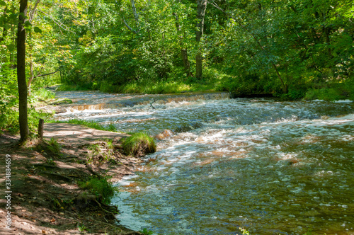 Wide view of small Baird Creek waterfall and rapids, flowing over the Niagara Escarpment at Baird Creek, Baird Creek Parkway, Green Bay, WI. Spring, summer rushing water.