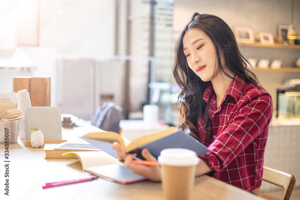 Young beautiful Asian woman reading a book while doing her homework in the modern co working space Young beautiful Asian woman reading a book while doing her homework in the modern co working space