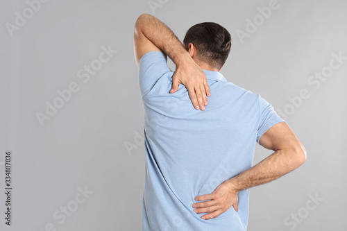 Man suffering from pain in back on light grey background. Visiting orthopedist