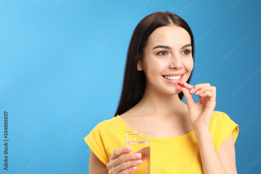 Young woman with glass of water taking vitamin capsule on light blue background. Space for text Young woman with glass of water taking vitamin capsule on light blue background. Space for text