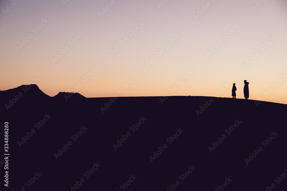 Berber desert silhouettes, father and son watching the dune landscape at sunset