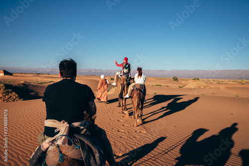 tourists led by a Moroccan Berber while riding camels in the middle of the desert on a sunny day