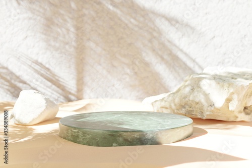 Round green marble podium and rocks on sand with palm tree shadow in the background. 3d rendered illustration. Best for product presentation.