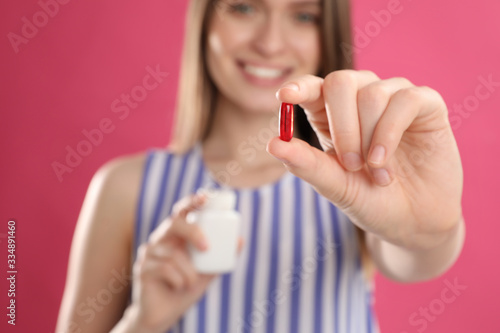 Young woman with vitamin pill against pink background, focus on hand