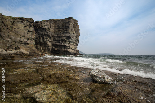 seashore with stones of volcanic rock, sheer cliffs, sunny day blue sky with cirrus clouds