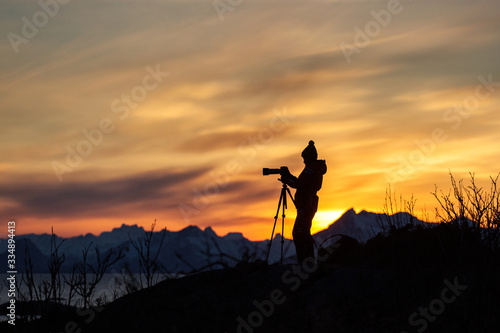 Photographer enjoying and taking pictures at beautiful landscape with mountains and colourful clouds at sunset in background. Lofoten Island  Norway.