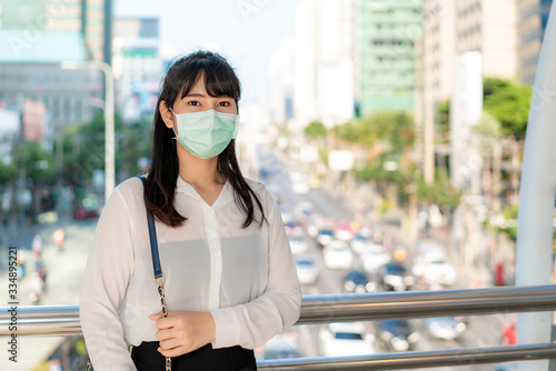 Young stress Asian businesswoman in white shirt going to work in pollution city she wears protection mask prevent PM2.5 dust, smog, air pollution and COVID-19 with traffic jam in Bangkok, Thailand.