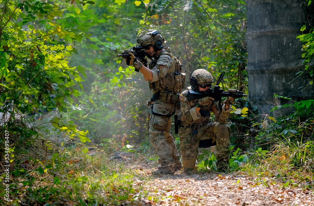 Two soldiers with the fighting uniform sit on the ground and discuss together for the battle in jungle.