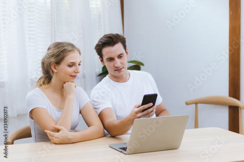 Smiling caucasian couple using smartphone for webinar or online shopping, surfing social media at home. Happy lover working business or education learning via phone Entrepreneur & work at home concept