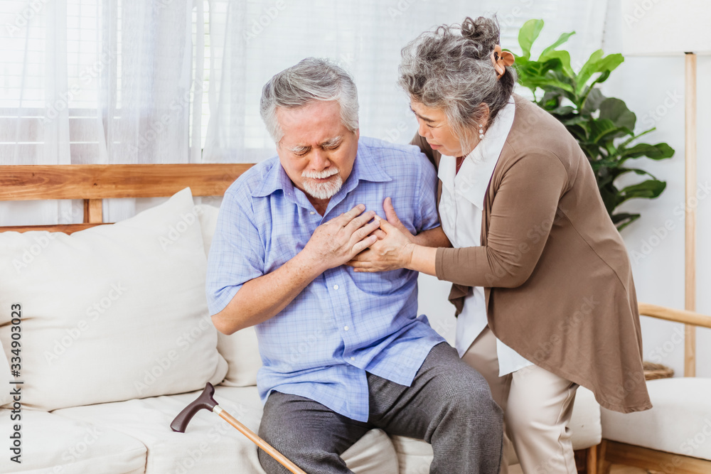 Obraz premium Retired Asian senior elderly husband pain from heart attack disease or illness with serious or worried wife take care at home. Medical emrgency treatment and health care insurance protection concept