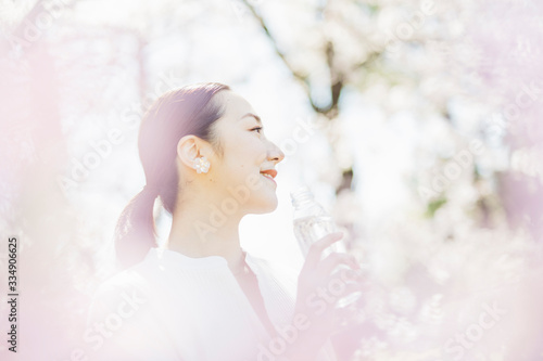 桜満開の中、水を飲むミドル女性