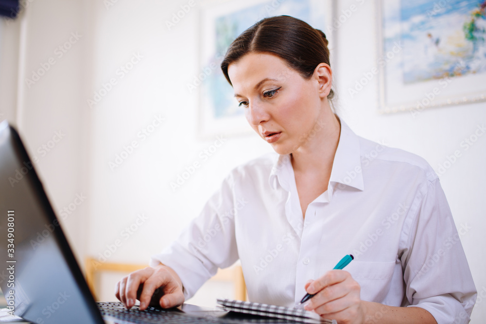 Millennial mixed-race woman looks at a laptop screen, listens to an educational webinar, takes notes, and receives remote online education at home. Millennial mixed-race woman looks at a laptop screen, listens to an educational webinar, takes notes, and receives remote online education at home.