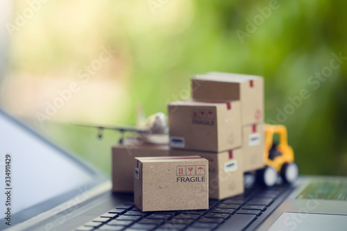 Logistic and cargo freight concept: Fork-lift a truck moves a paper box on notebook keyboard in the natural green background. depicts International freight or shipping service for online shopping.