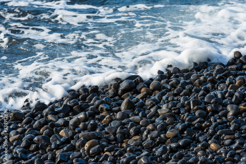 Black volcanic pebbles and deep blue water. Closeup, detail shot of the black pebbles at Mavra Volia beach on Chios. photo